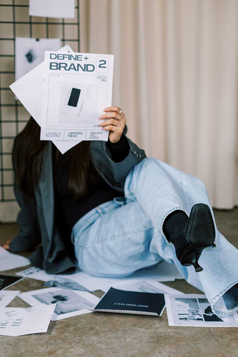 Person holding a ‘Define + Brand’ workbook with printed brand design materials on the floor